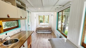 A compact, modern interior with a kitchenette, a bed, and large windows offering natural light and views.