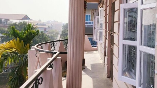 Un balcón con una columna, barandilla y vistas a edificios y árboles.