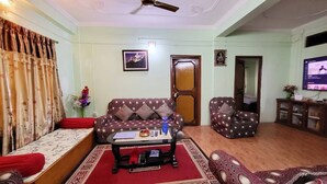Una sala de estar con sofá, sillón y mesa de centro, una televisión y una puerta.