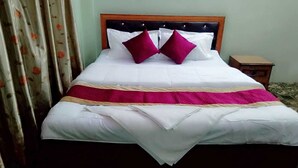 Una cama bien hecha con cabecera de madera, ropa de cama blanca y dos almohadas rojas.