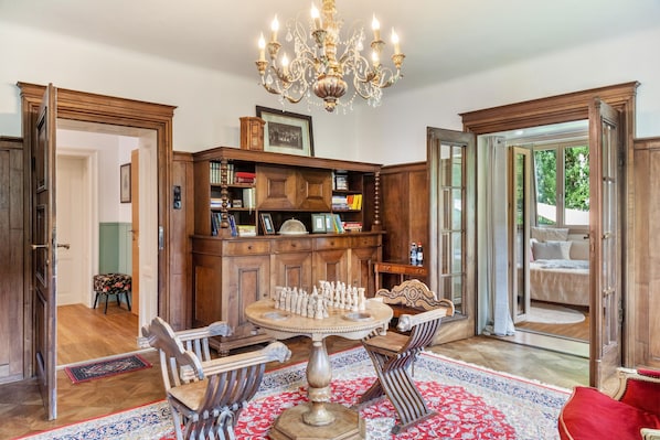 A room with a wooden bookcase, a chess table, and a chandelier.