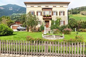 Ein großes, zweistöckiges Haus mit Vorgarten, Springbrunnen und Holzzaun.