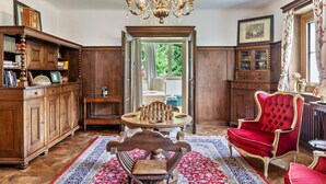 A room with a wooden cabinet, a red velvet chair, a chandelier, and a chessboard. - Apartment 'Villa Stumm' with Mountain View, Shared Terrace and Wi-Fi (Stumm)