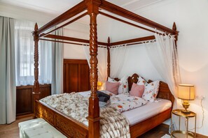 A four-poster bed with a canopy, a bedside table with a lamp, and a bench at the foot of the bed.