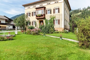 A two-story building with a balcony, surrounded by a well-maintained garden with a fountain and various plants.