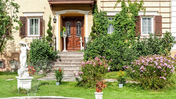 A building with a stone staircase leading to a wooden door, surrounded by lush greenery and a fountain. - Apartment 'Villa Stumm' with Mountain View, Shared Terrace and Wi-Fi (Stumm)