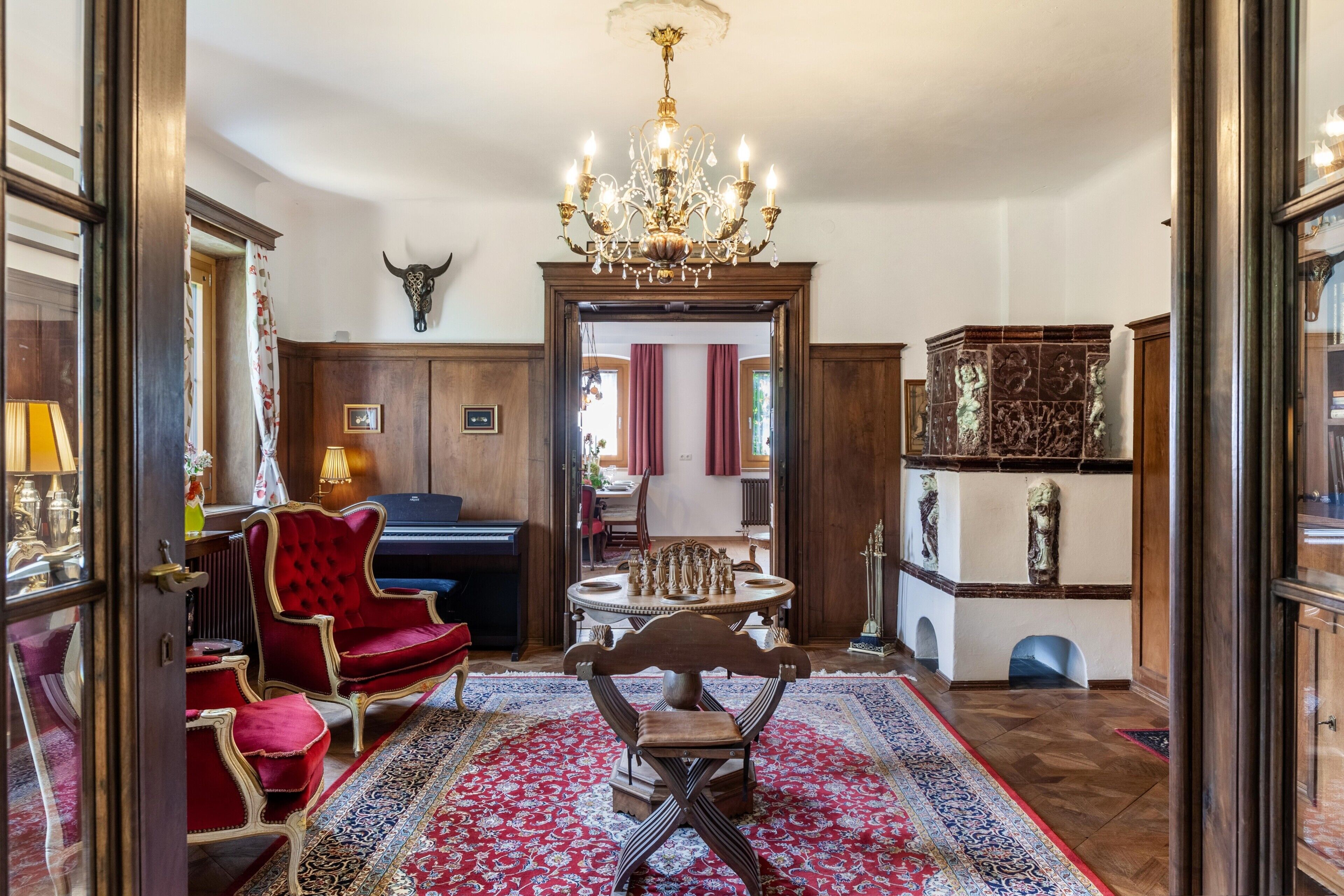 Una sala sontuosa con un lampadario, poltrone in velluto rosso, una scacchiera e un tappeto decorato.