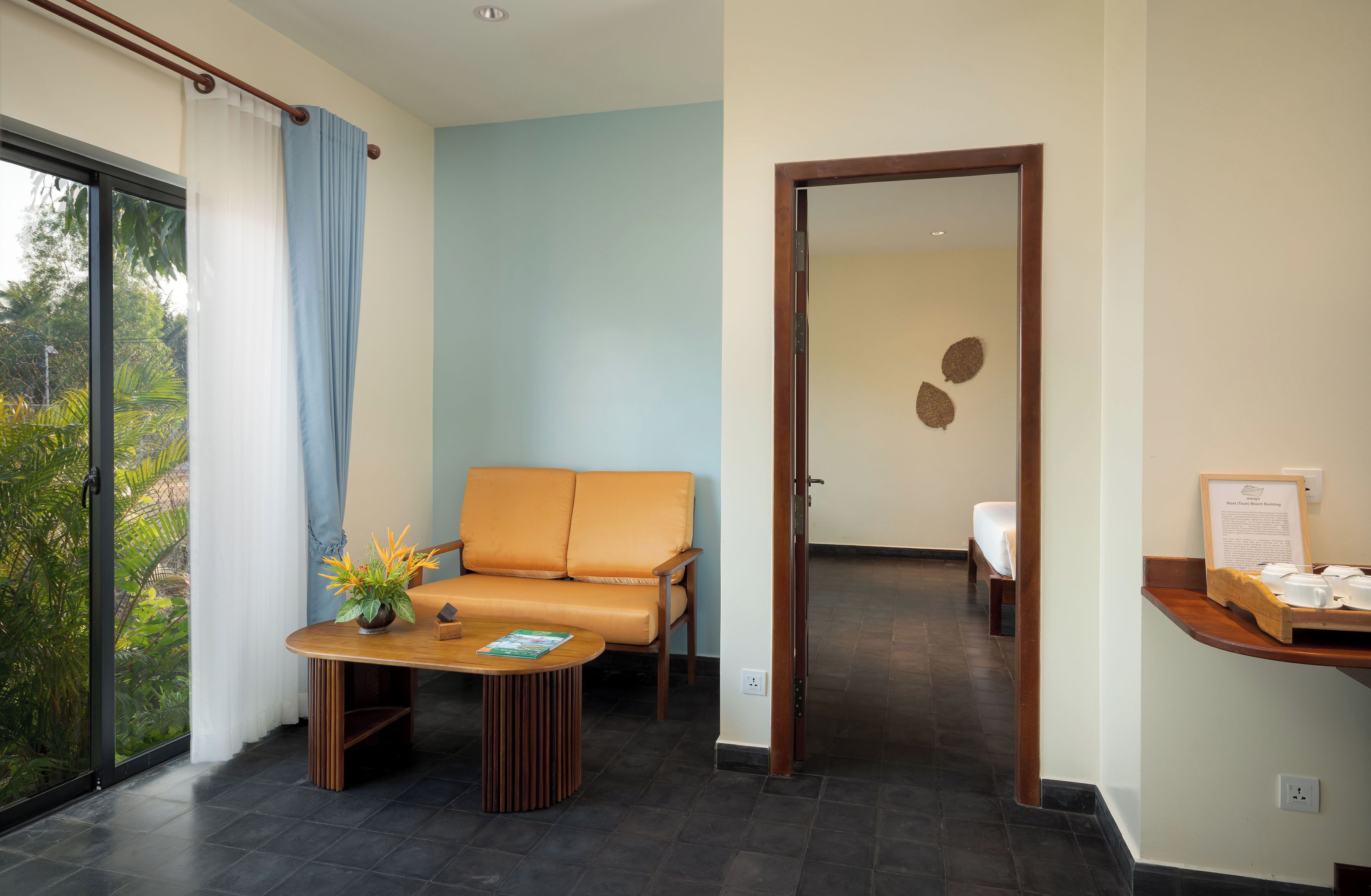 Una habitación moderna con sofá, una mesa con una planta, un escritorio de madera y vistas a la vegetación.