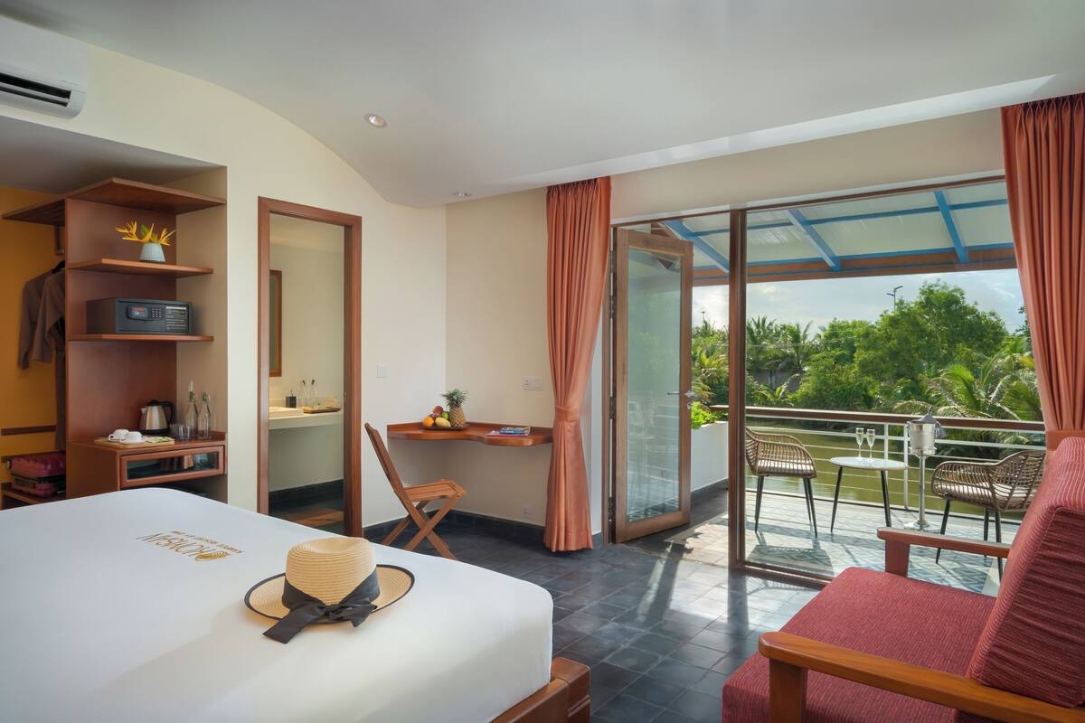 Ein Hotelzimmer mit Bett, Schreibtisch, Stuhl und einem Balkon mit Blick ins Grüne.