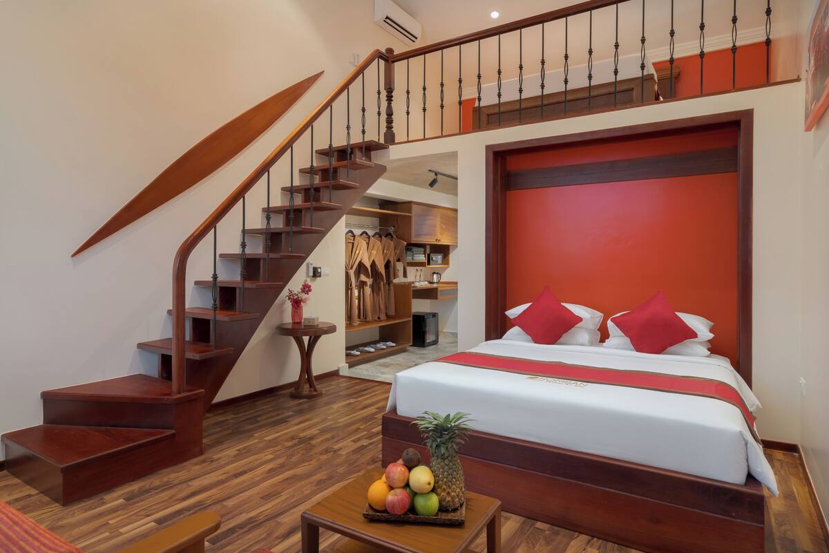 Ein Hotelzimmer mit einer Holztreppe, einem Bett mit roten Kissen und einer Obstschale auf einem kleinen Tisch.