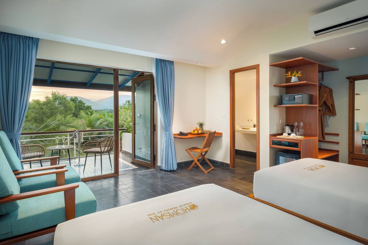 Ein Hotelzimmer mit zwei Betten, einem Schreibtisch und einem Balkon mit Sitzgelegenheiten.