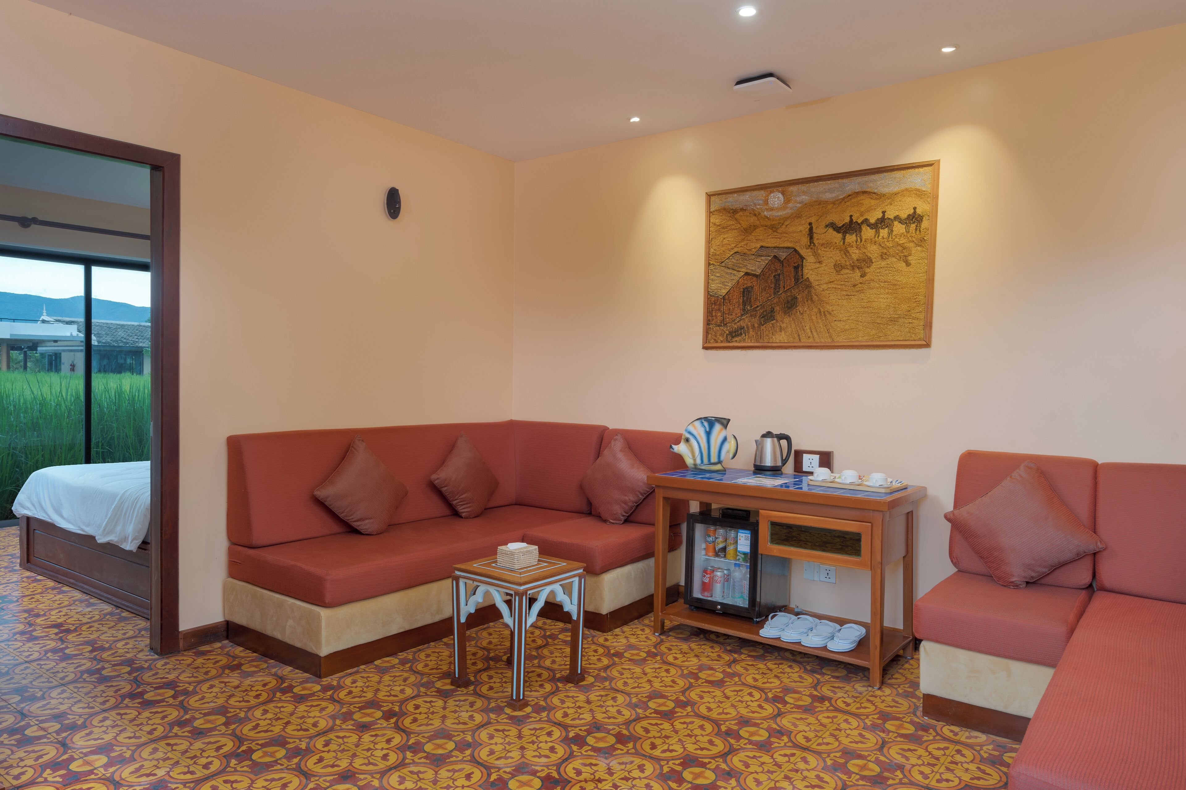 Ein Zimmer mit einem Bett, zwei Sofas, einem kleinen Tisch mit einem Wasserkocher, einem Kühlschrank und einem Bild an der Wand.