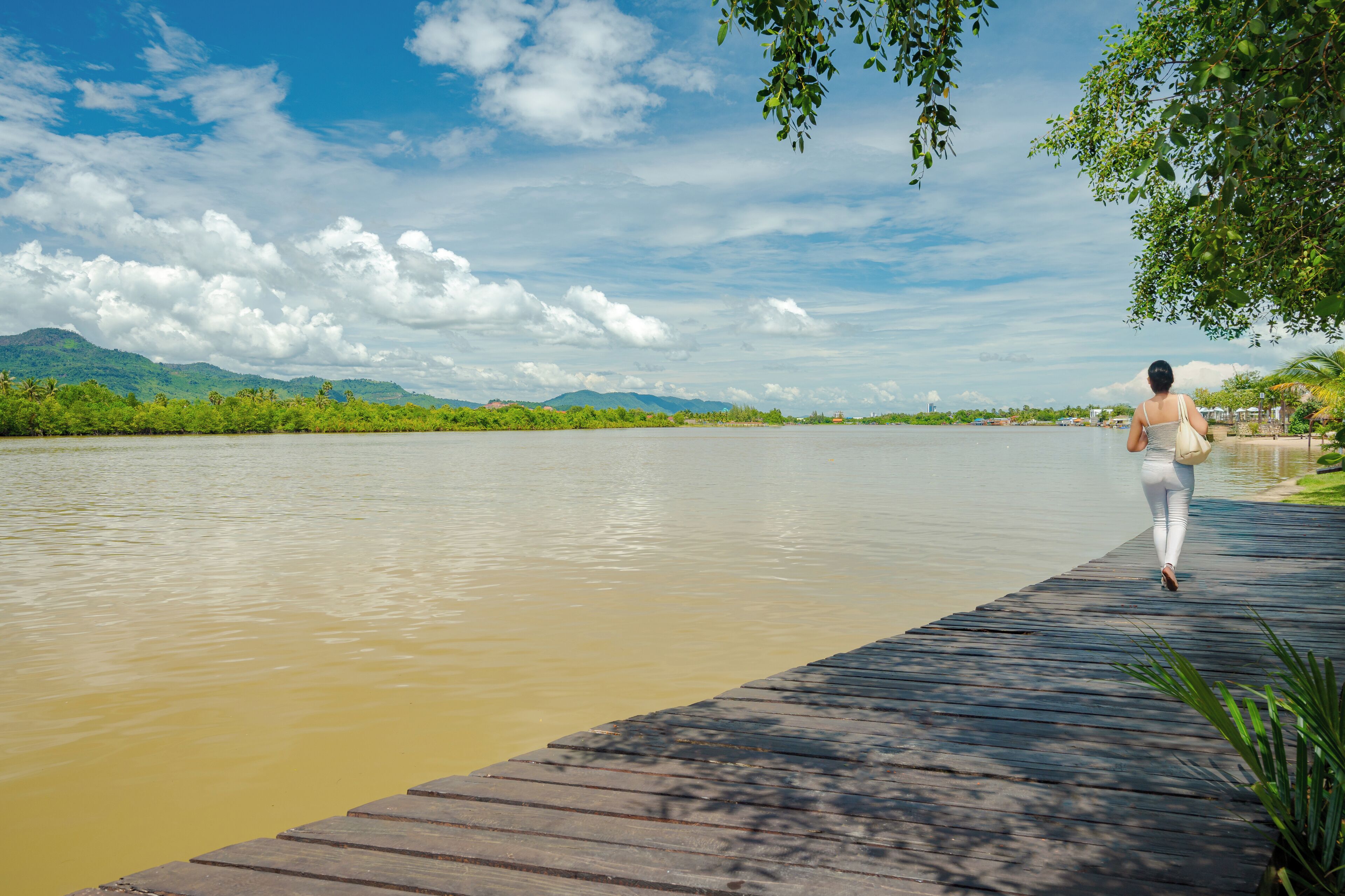 A wooden dock extending into a river with a person walking along it.