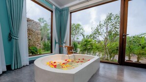 Ein modernes Badezimmer mit freistehender Badewanne, großen Fenstern und Blick ins Grüne.
