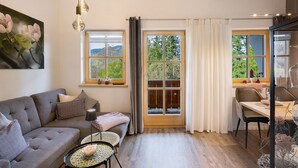 A modern living room with a sofa, a dining table, and a large window with curtains.