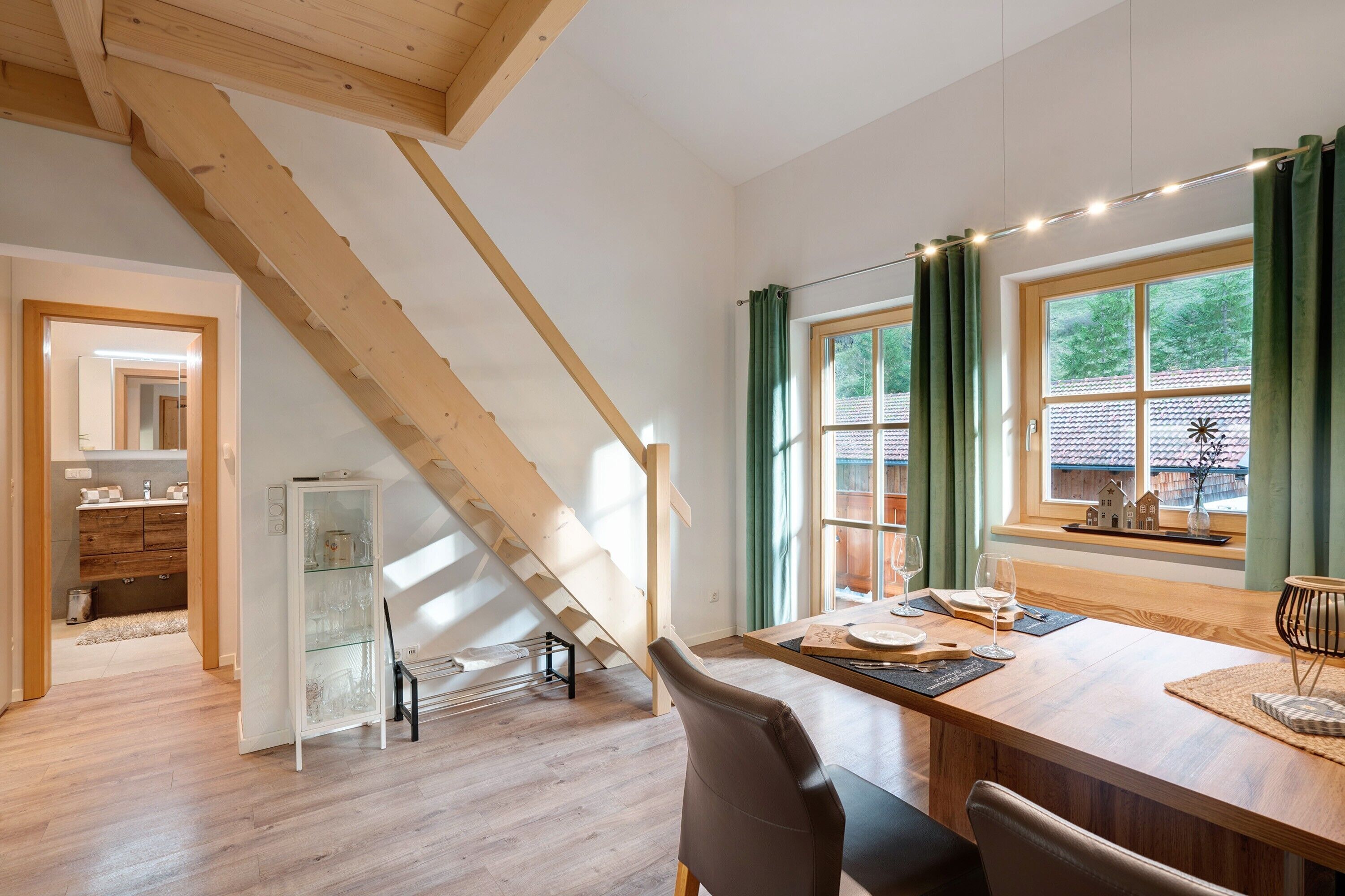 A dining area with a wooden table, chairs, a glass cabinet, and a staircase.