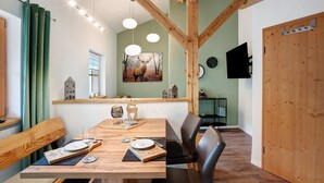 A dining area with a wooden table, chairs, a painting of an elk, and a television mounted on the wall. - Apartment 'Ferienwohnung Unternberg' with Mountain View, Shared Terrace and Wi-Fi (Ruhpolding)