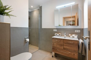 A modern bathroom with a toilet, shower, vanity with a mirror, and a potted plant.