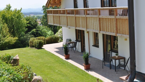 A two-story building with a balcony, outdoor seating, and a view of the landscape.
