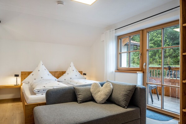A bedroom with a bed, a sofa, a window, and a balcony.