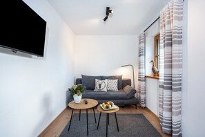 Uma sala de estar moderna com televisão de tela plana, sofá cinza, duas mesas de centro redondas, uma planta em vaso e cortinas listradas.