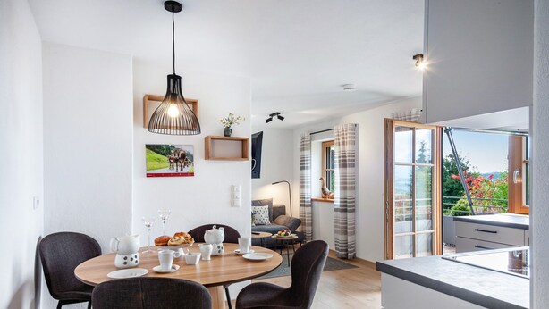A modern dining area with a round table, chairs, and a hanging light fixture.