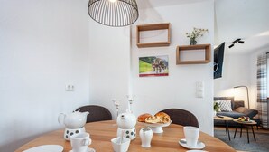 A dining area with a round table, white tableware, a teapot, and a loaf of bread.
