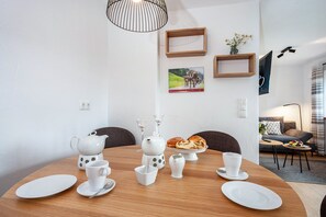 A dining area with a round table, white tableware, a teapot, and a loaf of bread.