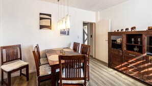 A dining area with a wooden table and chairs, a cabinet with decorative items, and a modern light fixture. - Holiday Home 'Lichtblick' with Private Terrace, Shared Garden, and Wi-Fi (Bottrop)