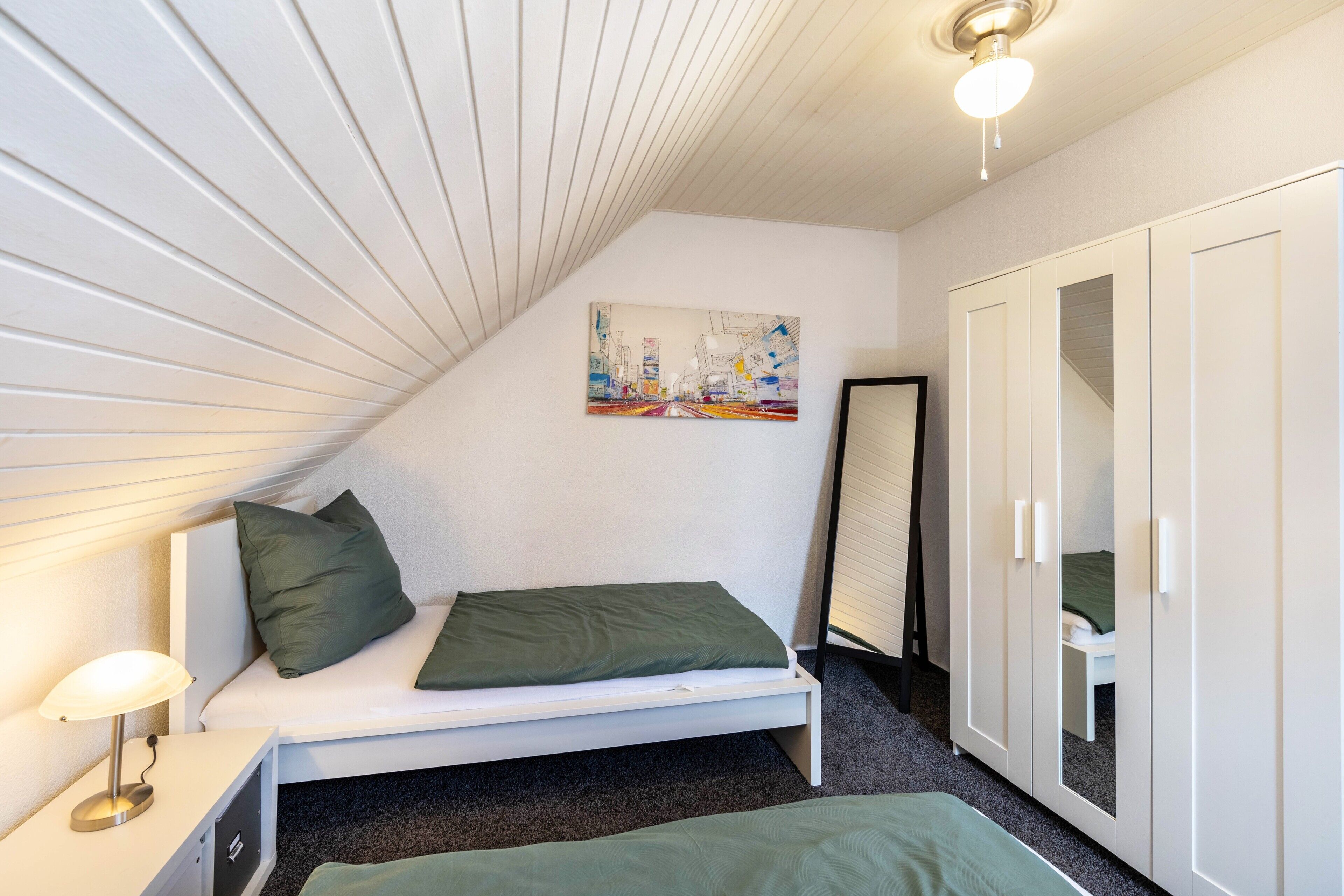 Une chambre à coucher avec un lit, une table de chevet, une lampe, un tableau au mur et une armoire.