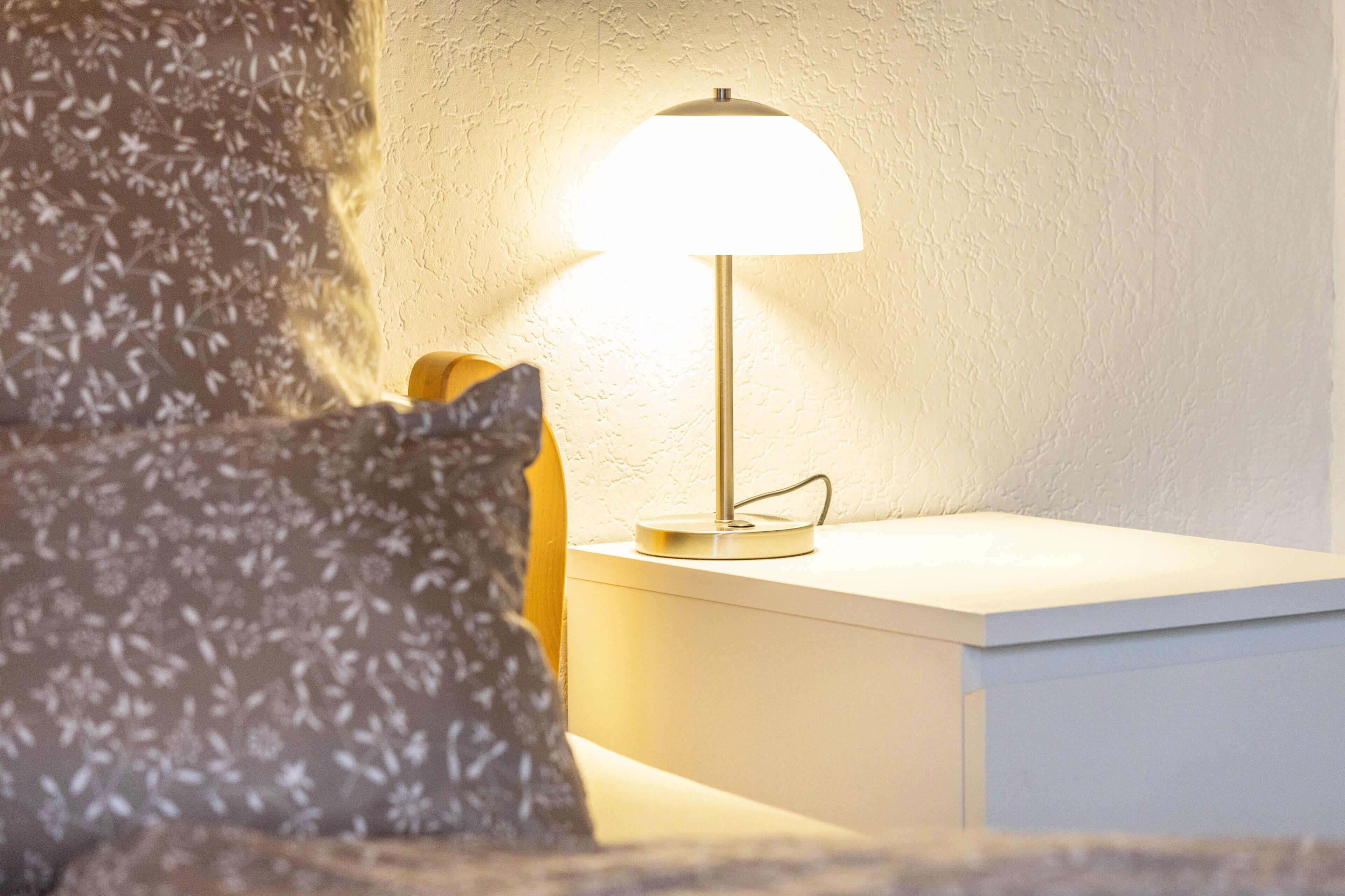 Eine Lampe auf einem Nachttisch mit einem blumigen Kissen.