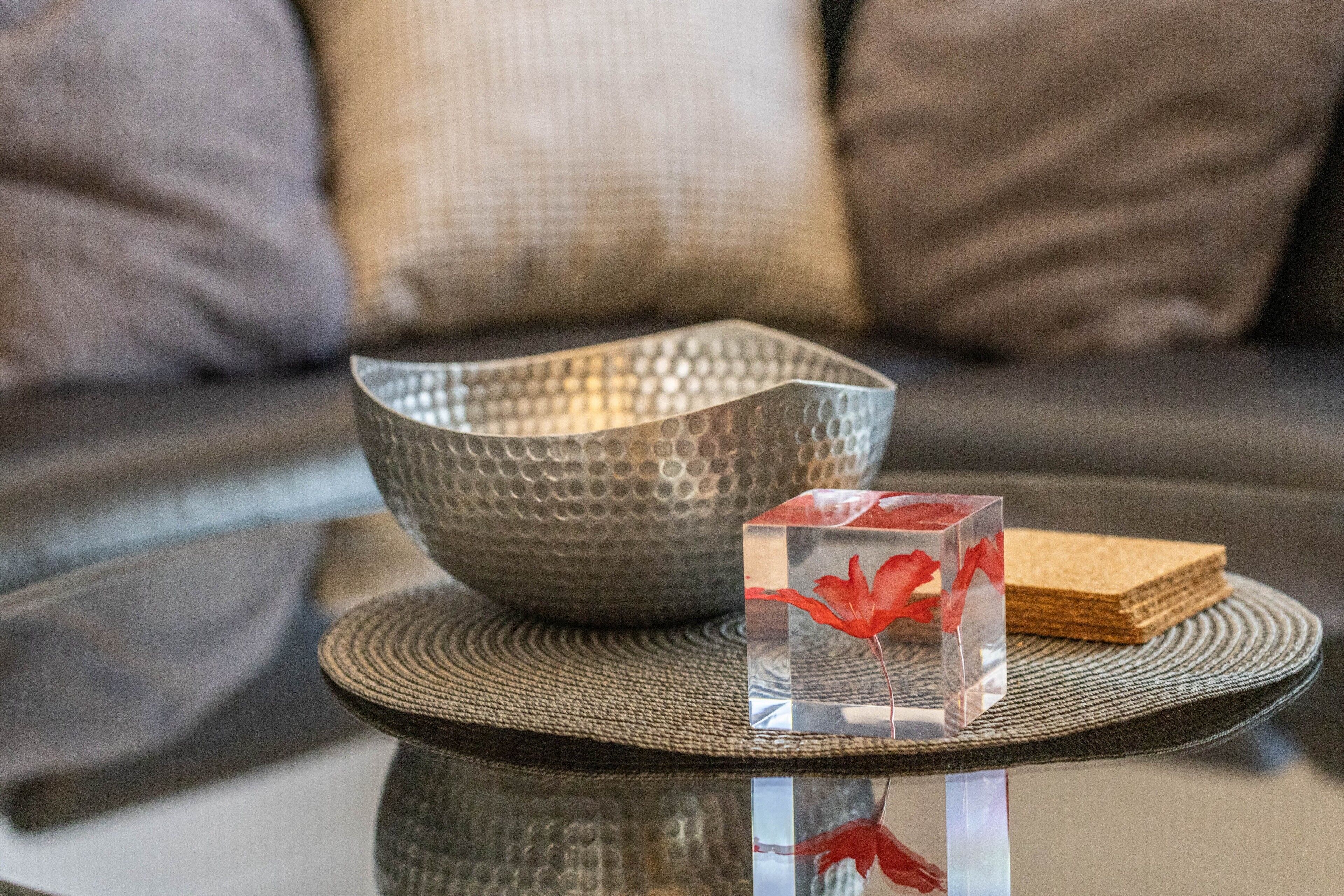 A glass table with a textured bowl and a clear cube with a red leaf.