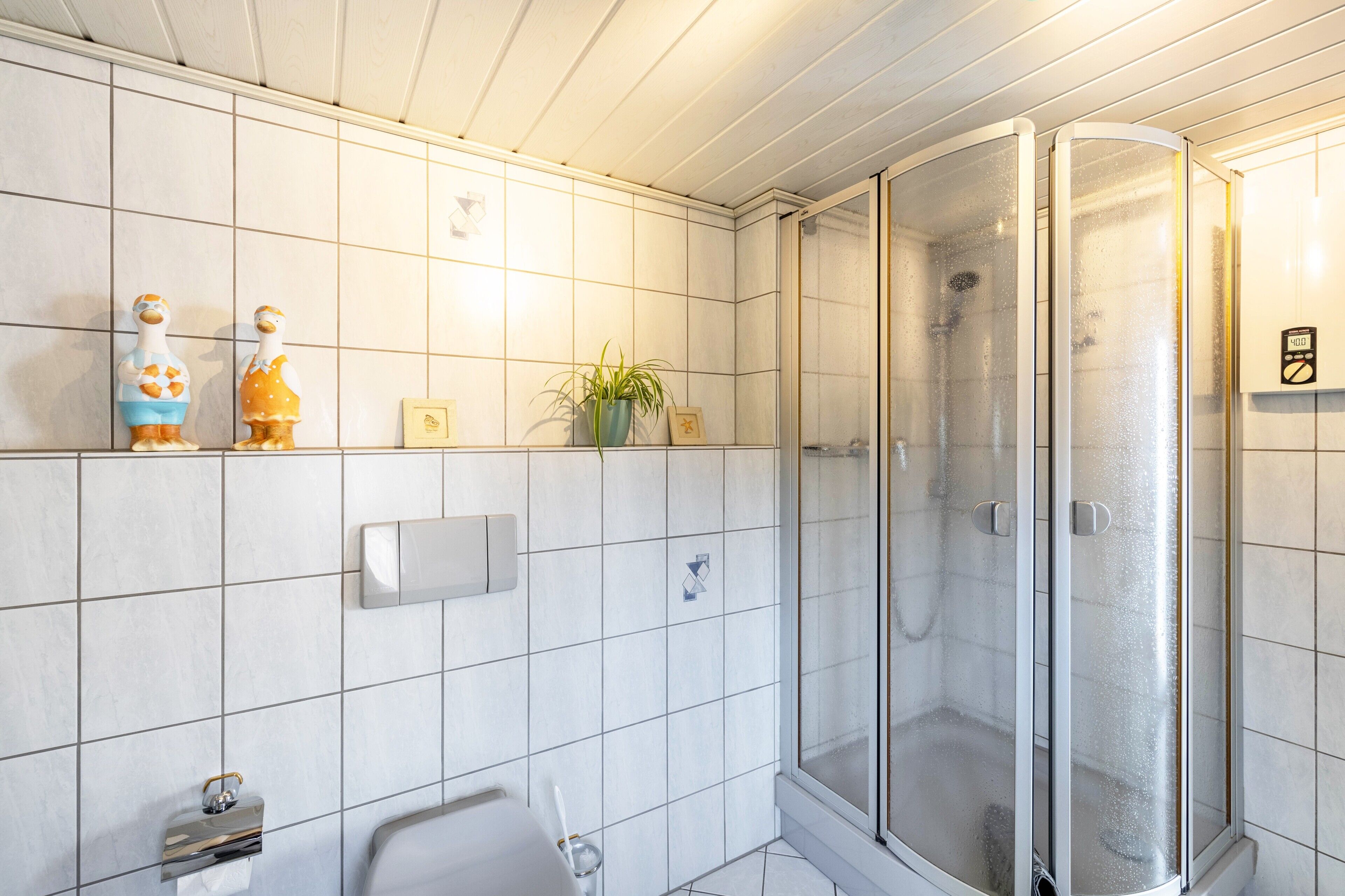 A bathroom with white tiles, a shower with frosted glass doors, a toilet, and two decorative bird figurines.