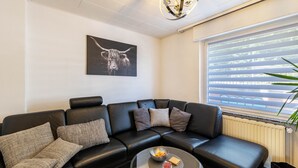 A modern living room with a black leather sofa, a glass coffee table, a framed artwork of a bull, and a window with blinds. - Holiday Home 'Lichtblick' with Private Terrace, Shared Garden, and Wi-Fi (Bottrop)