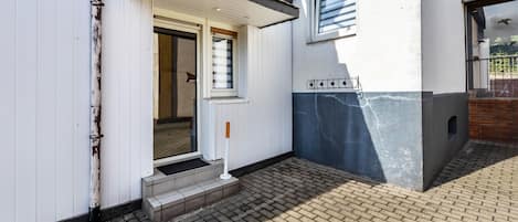 Ein Gebäude mit weißer Fassade, einem sichtbaren Eingang und einem von Ziegeln gepflasterten Vorplatz.
