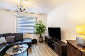A modern living room with a sofa, a coffee table, a TV, a potted plant, and a lamp. - Holiday Home 'Lichtblick' with Private Terrace, Shared Garden, and Wi-Fi (Bottrop)