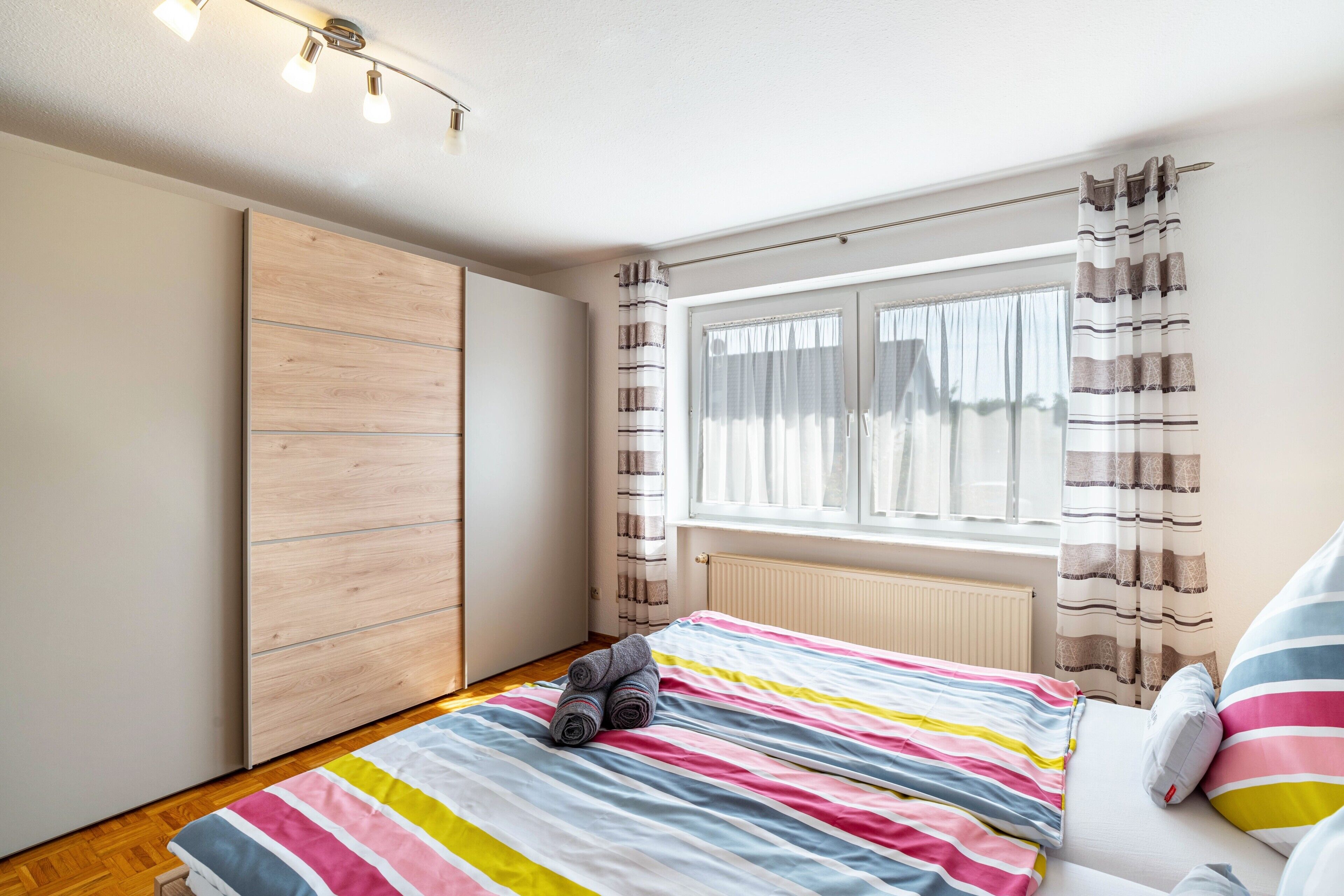 Ein Schlafzimmer mit einem Bett, einem Holzschrank, einem Fenster mit Vorhängen und einer Heizung.