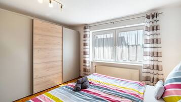 Ein Schlafzimmer mit einem Bett, einem Holzschrank, einem Fenster mit Vorhängen und einer Heizung.