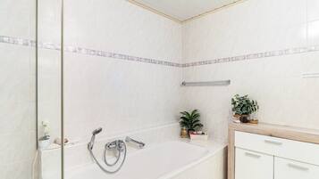 Een badkamer met een bad, een douche, een wastafel met spiegel en een kleine potplant.