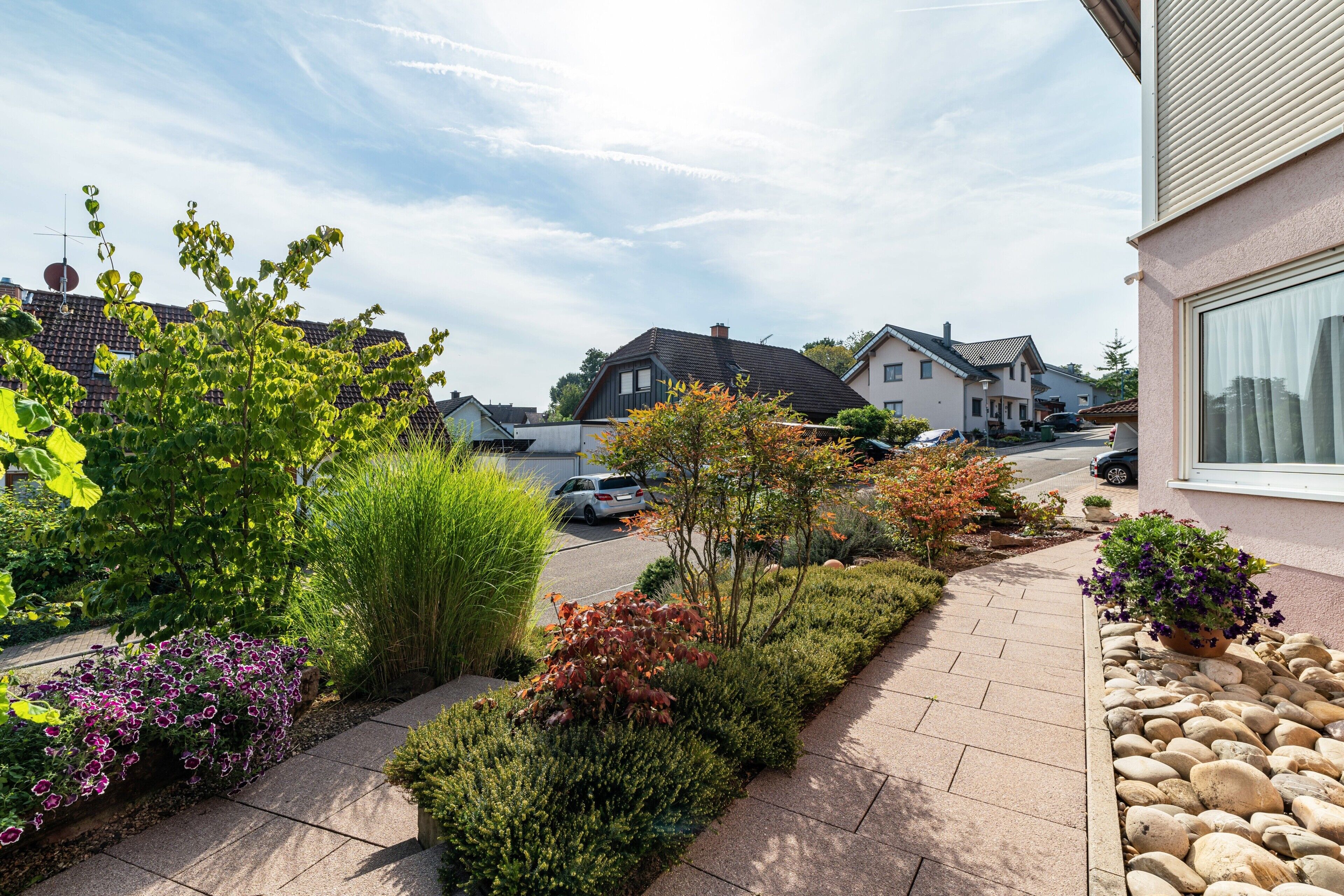 Une rue résidentielle bordée de maisons, avec un trottoir pavé et diverses plantes.
