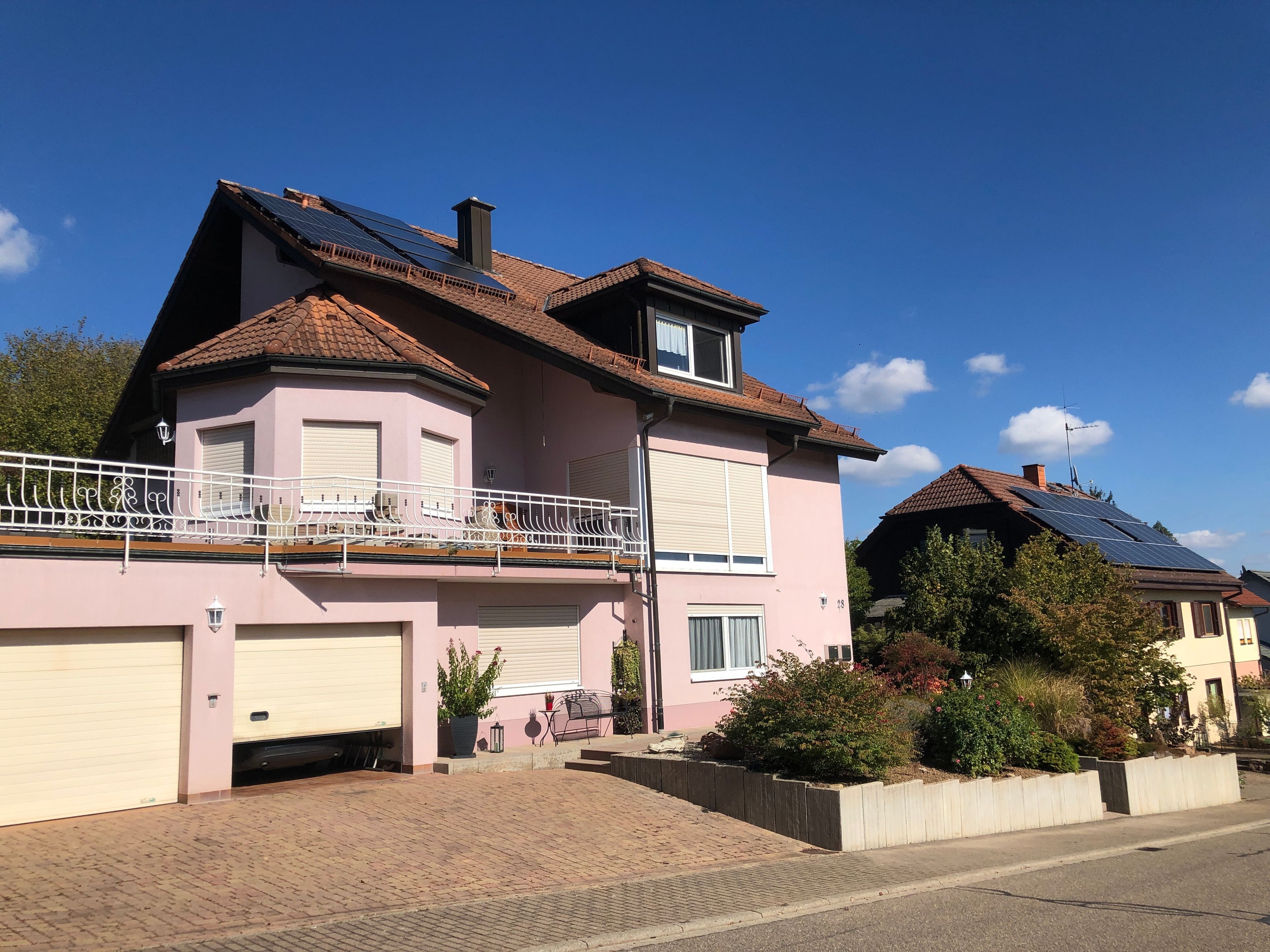 Une maison à deux étages avec un garage, un balcon et des panneaux solaires sur le toit.