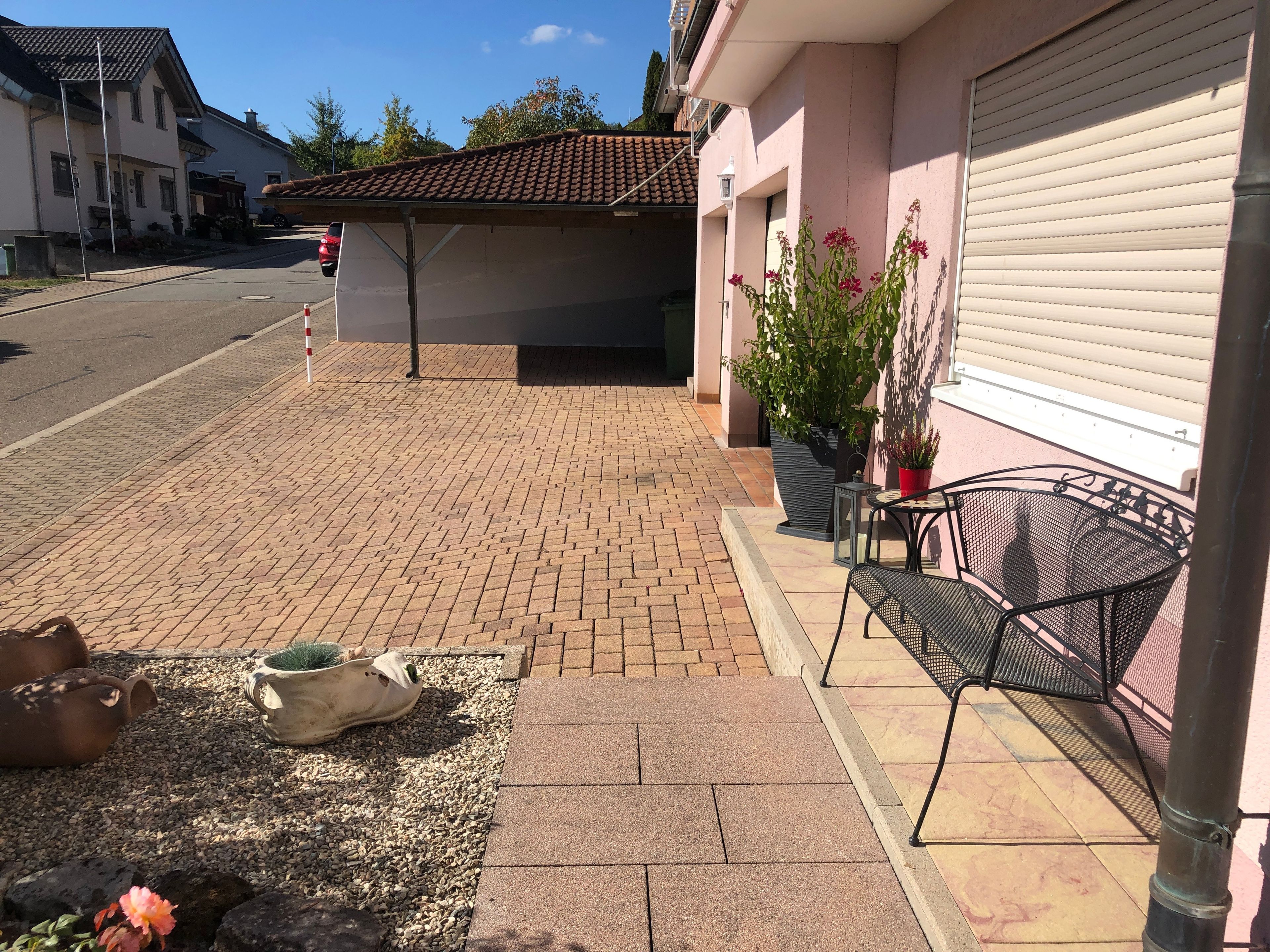 Un patio empedrado con una silla y una mesa de metal, plantas en macetas y la puerta de un garaje.