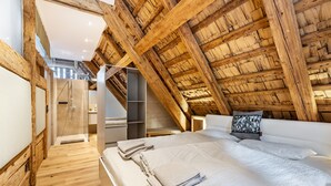 A bedroom with a sloped ceiling, wooden beams, a bed with white linens, and a walk-in closet.