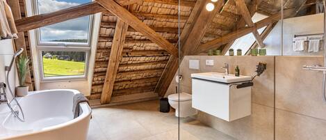 A rustic bathroom with a freestanding bathtub, a toilet, and a glass-enclosed shower area.