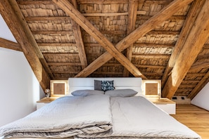 A bedroom with a wooden ceiling, a bed with a white headboard, two pillows, and a nightstand with a lamp.