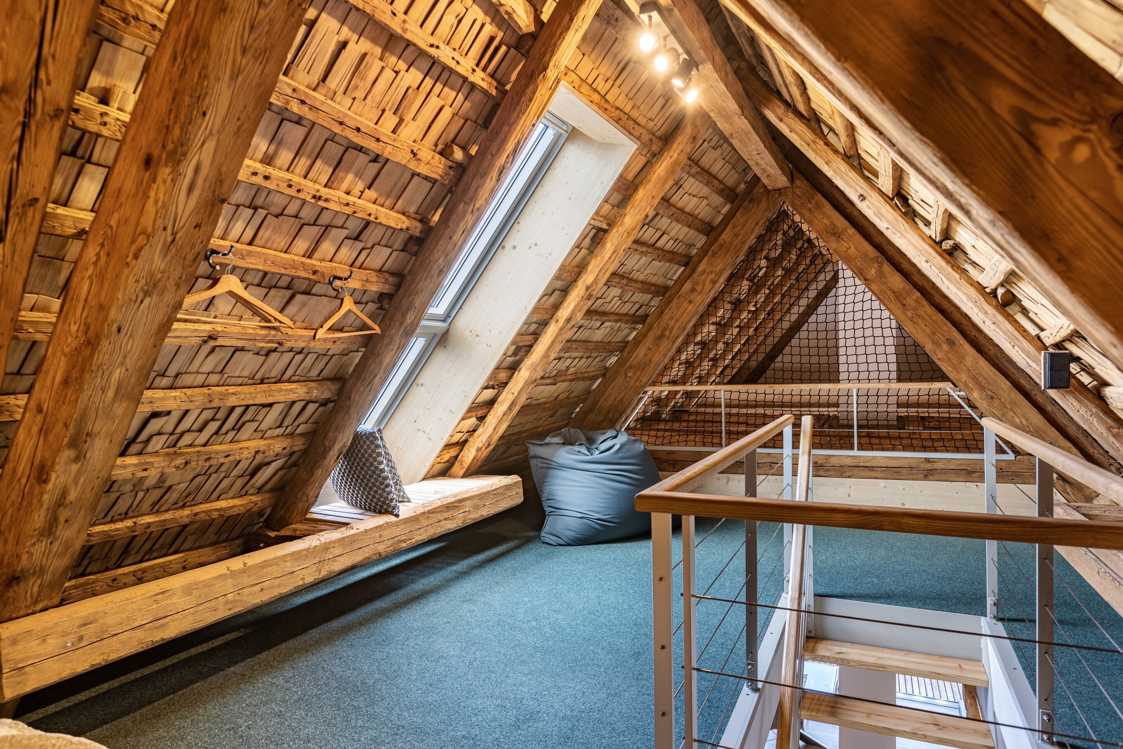 A high-ceilinged attic room with wooden beams, a skylight, and a view of the sky.