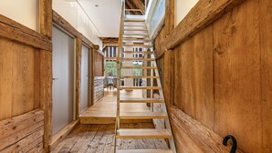A wooden interior with a central staircase, wooden walls, and a view into a dining area.