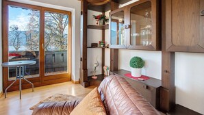 A room with a wooden ceiling, a glass door leading to a balcony, a brown leather sofa, and a wooden cabinet with glass doors.