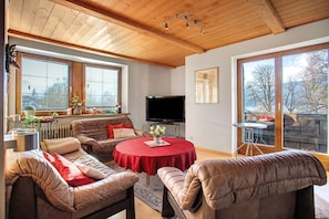 A living room with a wooden ceiling, a television, a red table, and a view of the outdoors.