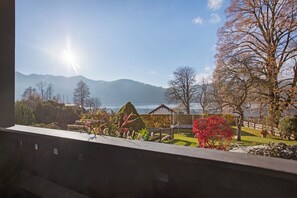 A view from a window overlooking a garden with a lake and mountains in the distance.